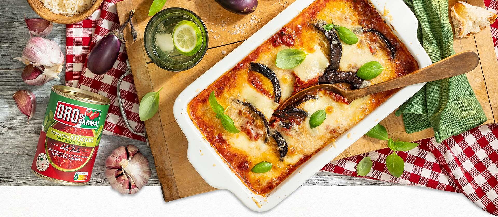 Ein Teller mit Auberginen-Auflauf, daneben Messer, Gabel und eine graue Serviette.