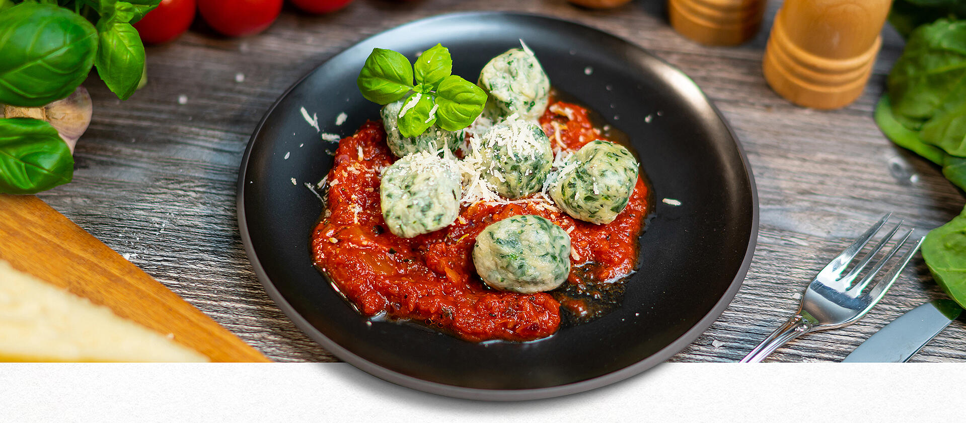 Gnudi in Tomatensauce auf einem schwarzen Teller, mit Basilikum garniert