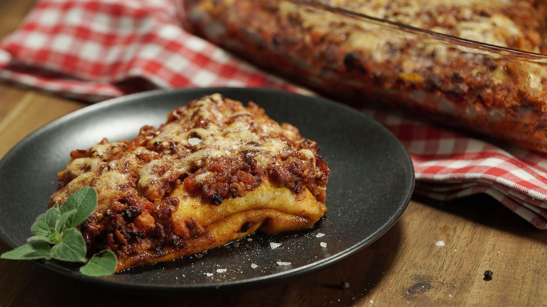 Crespelle - italienische Pfannkuchen gefüllt mit Bolognese auf einem schwarzen Teller