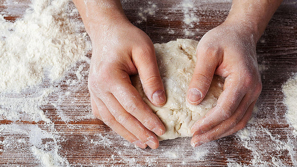 Zwei Hände kneten Pizzateig