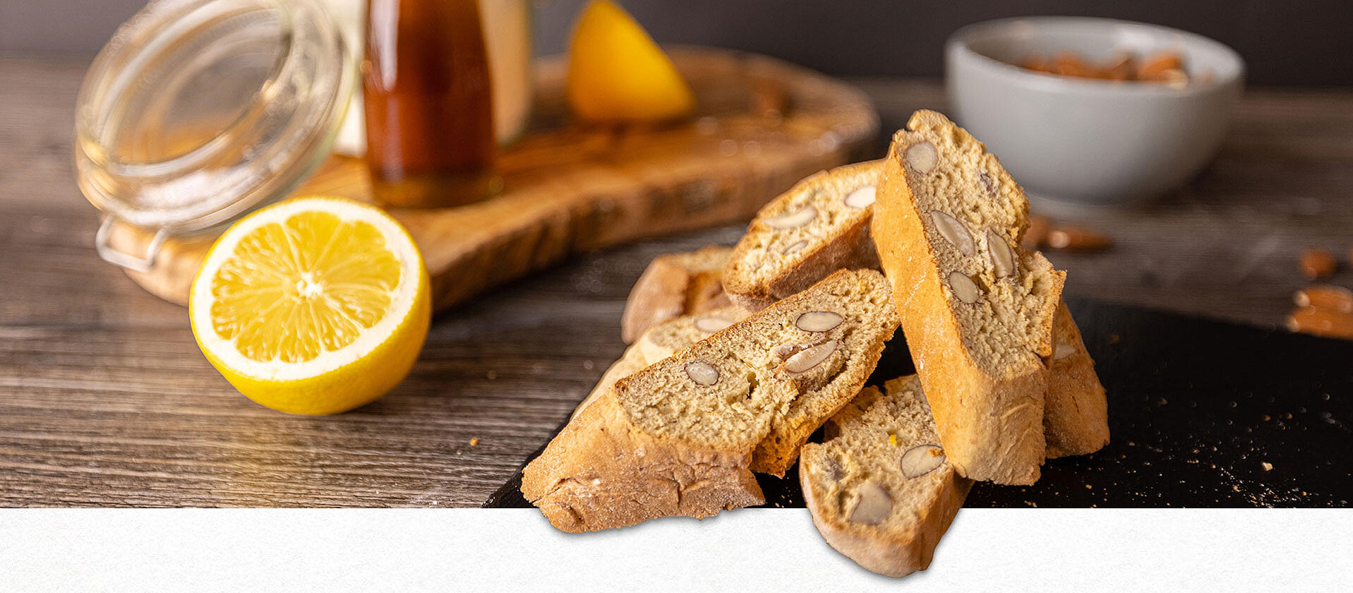 Auf einer Schieferplatte liegen 4 italienische Cantuccini. Im Hintergrund eine Tasse Kaffee.