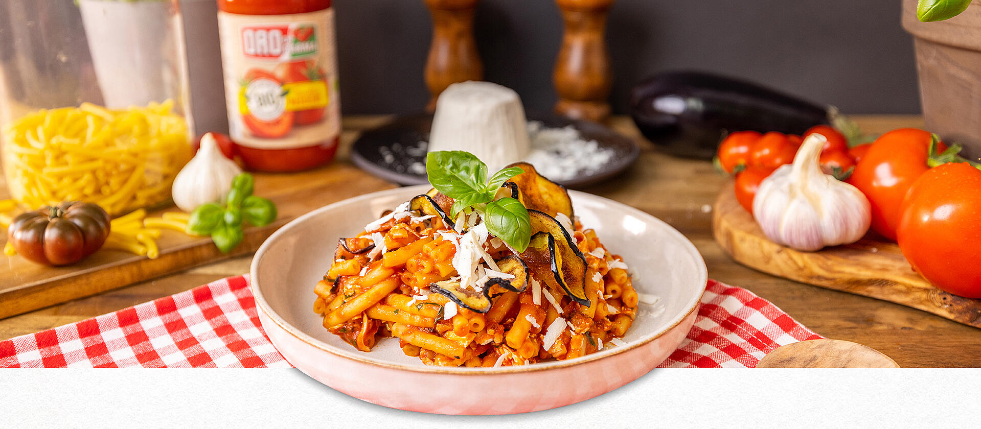 Pasta alla Norma mit Auberginenchips auf einem weißen Teller angerichtet