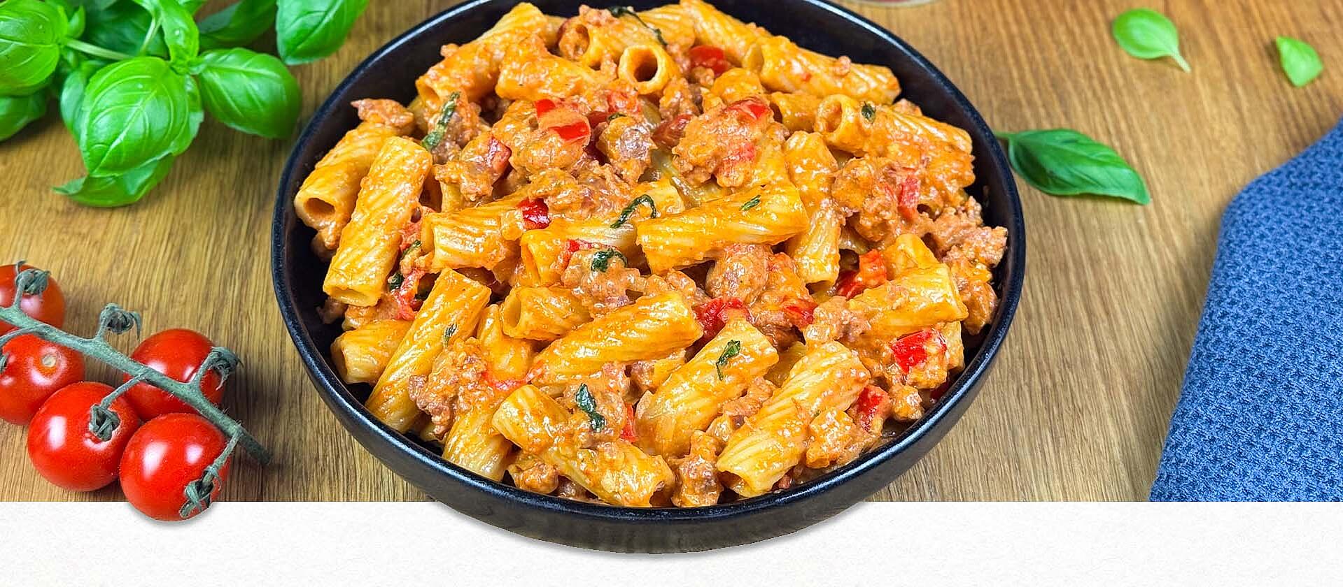 Ein Teller gefüllt mit cremiger Salsiccia Pasta und umgeben von frischem Basilikum und Tomaten 