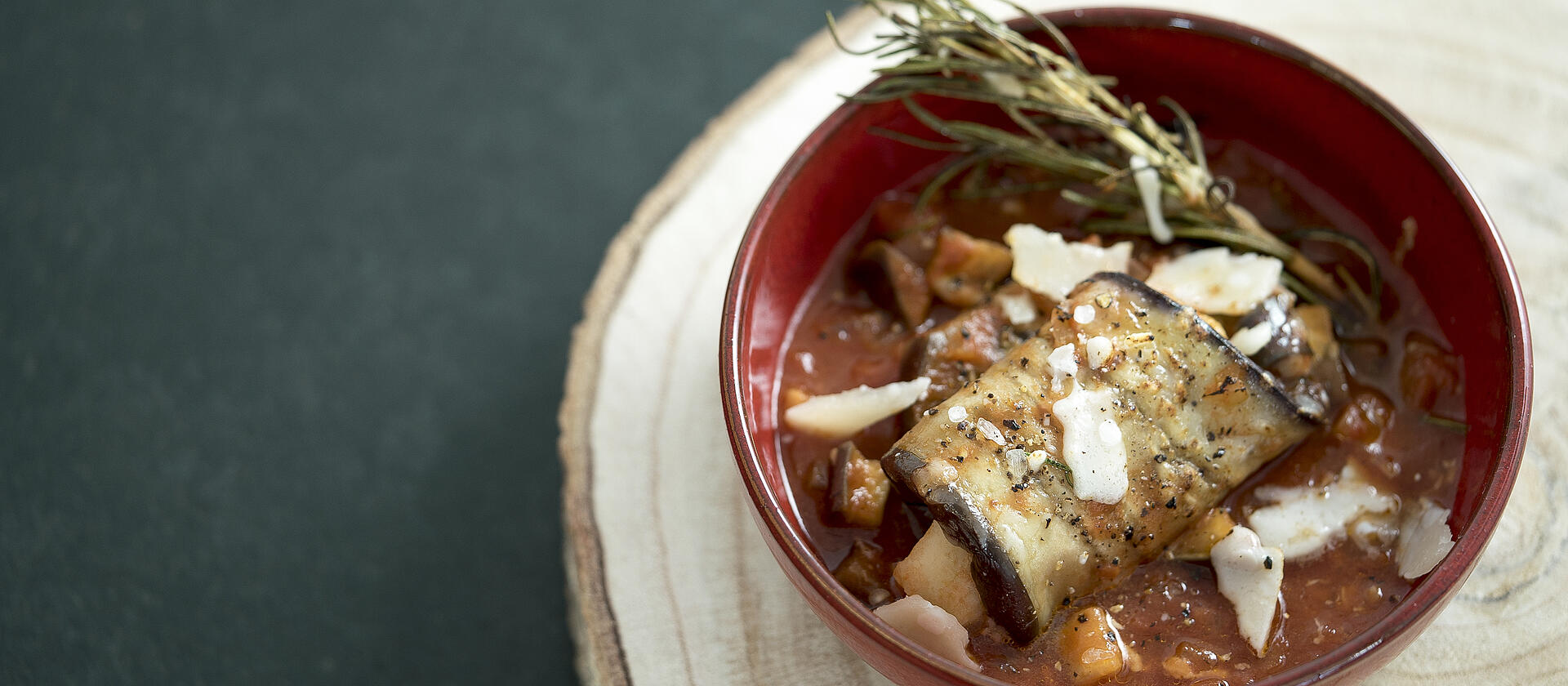 Braised eggplant rolls in a red bowl.