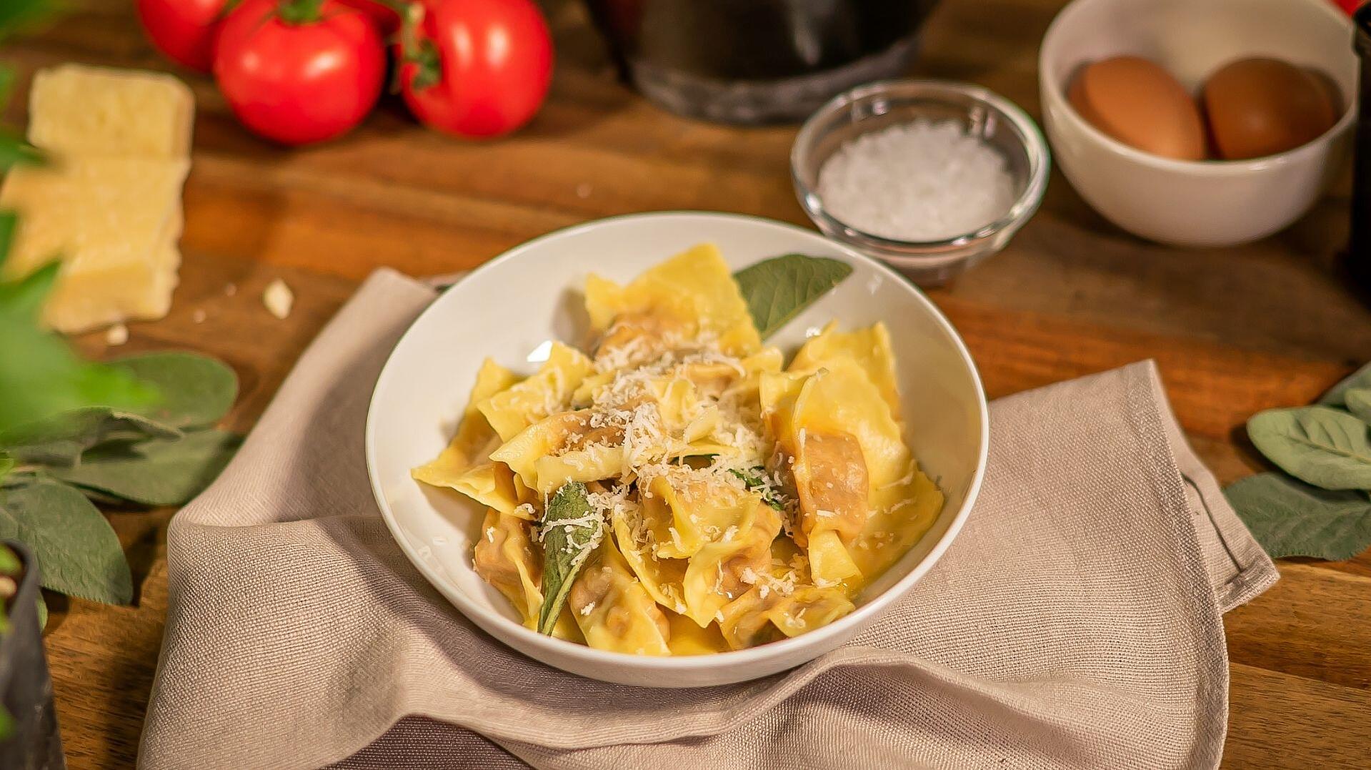 In einer weißen Schüssel sind italienische Agnolotti zu sehen. Die Schüssel steht auf einem beigen Küchentuch. 