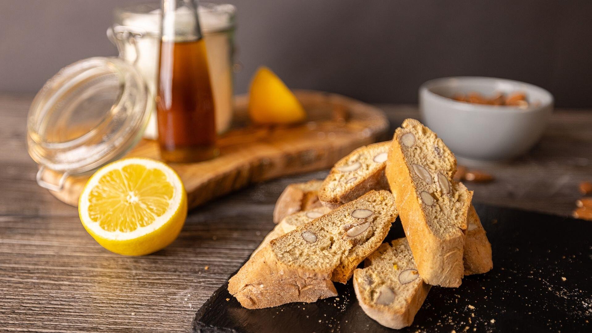 Auf einer Schieferplatte liegen 4 italienische Cantuccini. Im Hintergrund eine Tasse Kaffee.