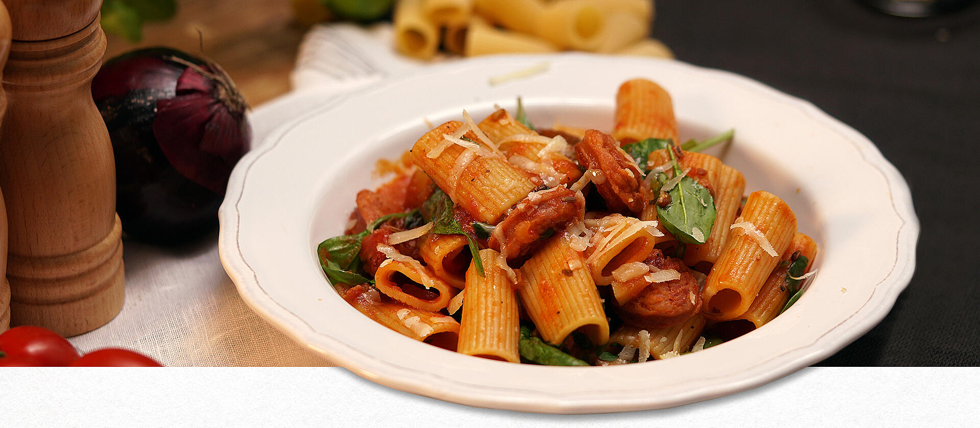 Rigatoni-Nudeln mit Salsiccia-Tomatensauce auf einem weißen Pastateller