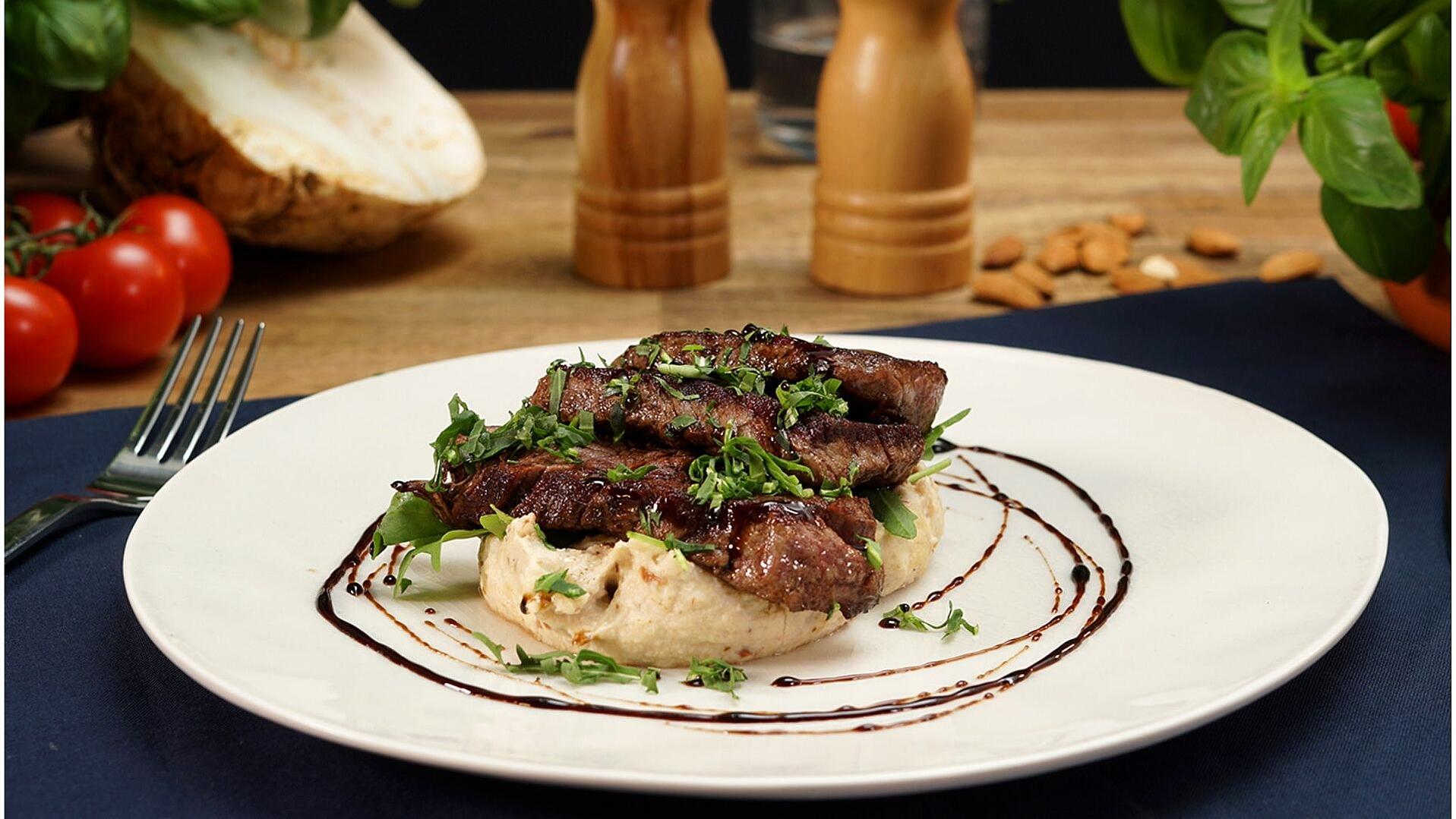 Ein Teller mit Sellerie-Pürree. Darauf wurden mehrere Scheiben Rinderfilet angerichtet und das Ganze mit Balsamico-Creme dekoriert