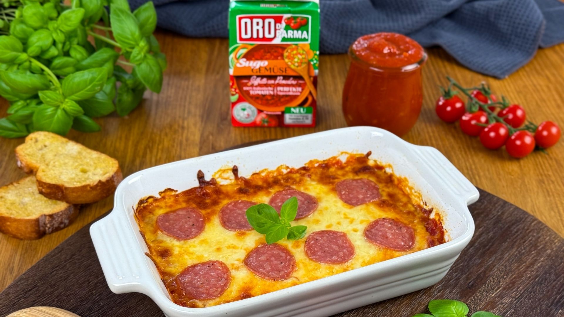 Pizzadip in Auflaufform mit Basilikum auf Holzbrett, dazu geröstetes Ciabatta.