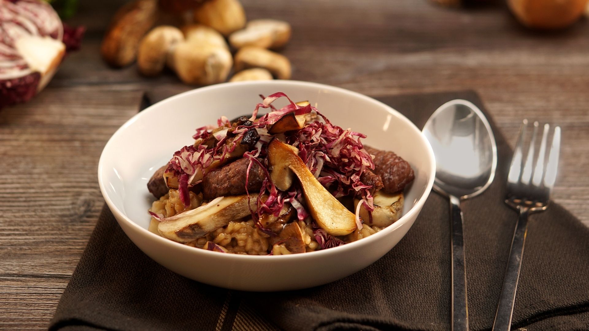Eine Schüssel gefüllt mit Steinpilzrisotto, rechts daneben ein Löffel und eine Gabel