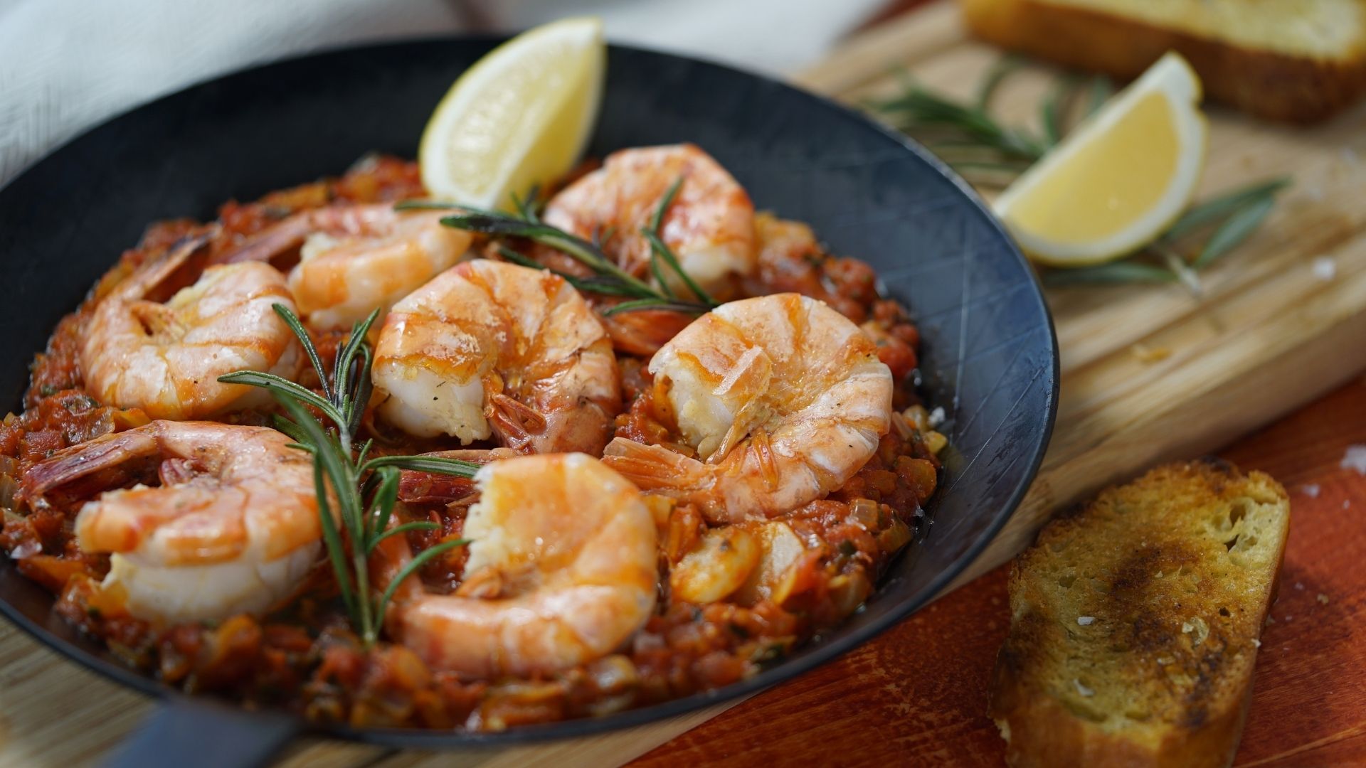 Riesengarnelen mit Tomatensauce, einem Zitronenviertel und Rosmarin auf einem Teller angerichtet