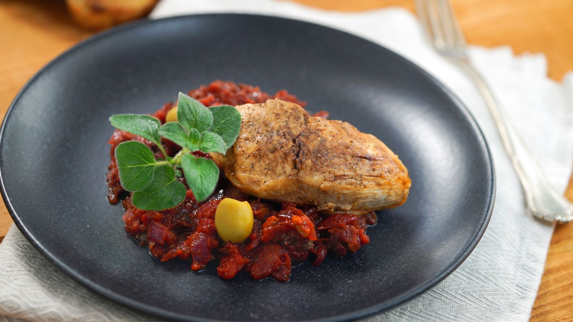 Ein schwarzer Teller mit Hähnchenbrust auf Tomaten-Oliven-Sauce 