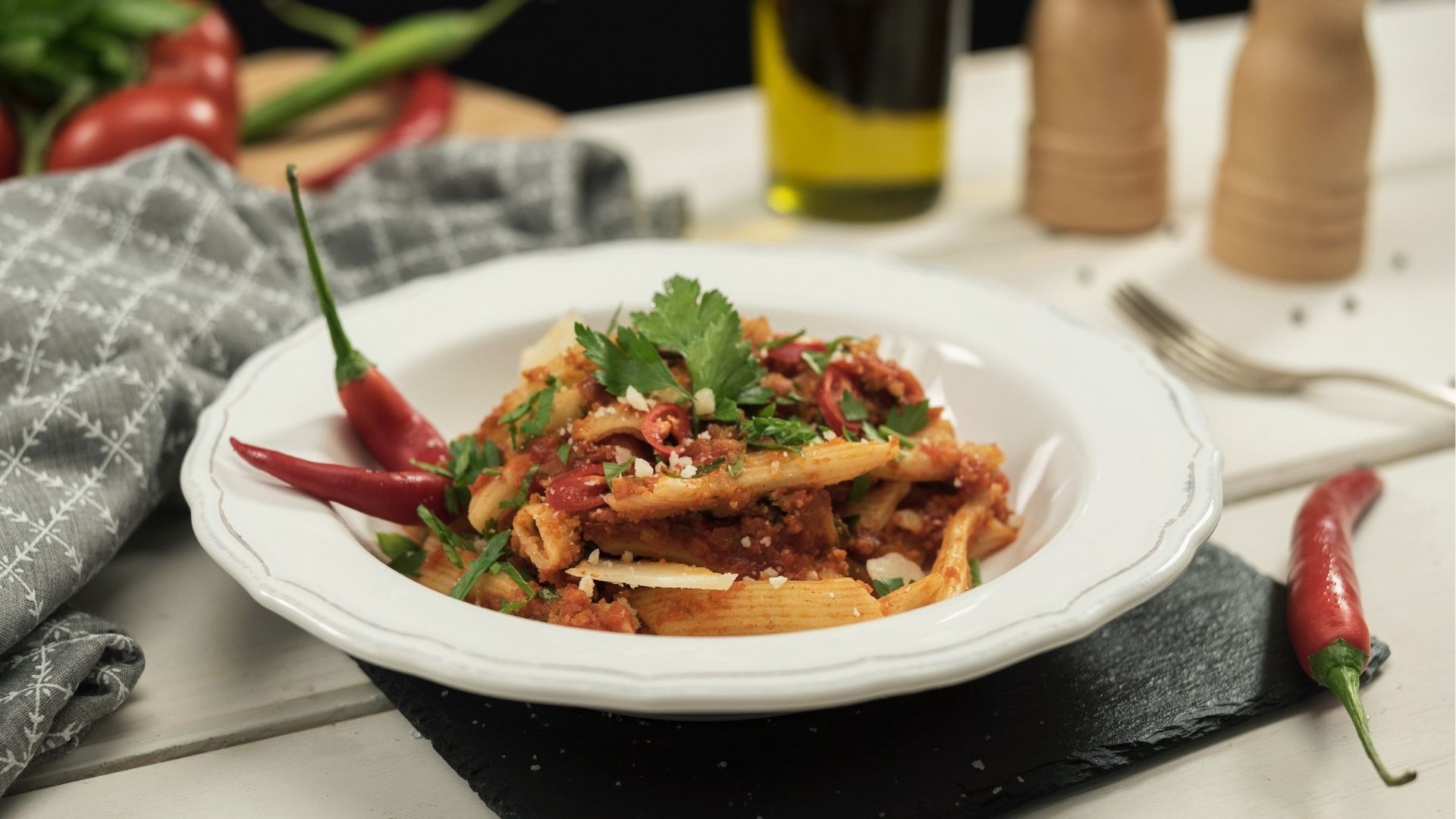 Penne all’arrabbiata auf einem weißen Pastateller mit Petersilie, geriebenem Parmesan und zwei Chilischoten garniert