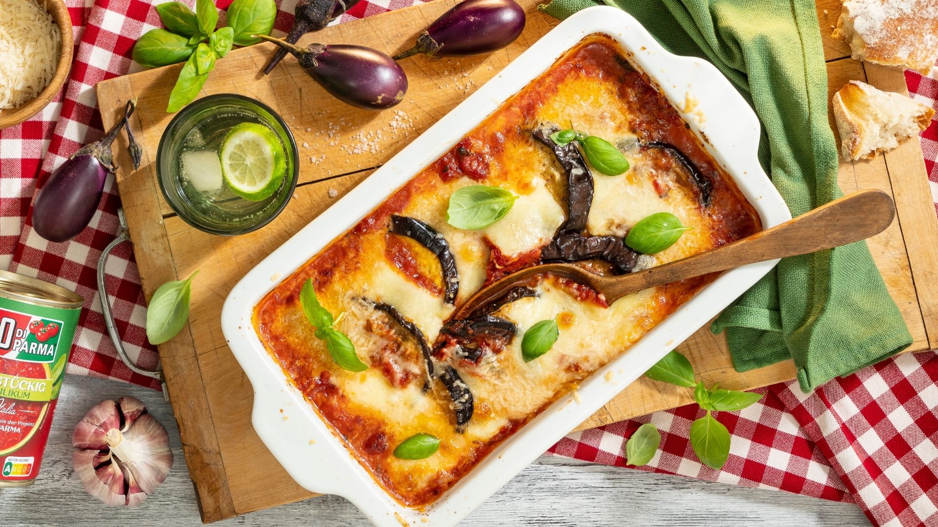 Ein Teller mit Auberginen-Auflauf, daneben Messer, Gabel und eine graue Serviette.