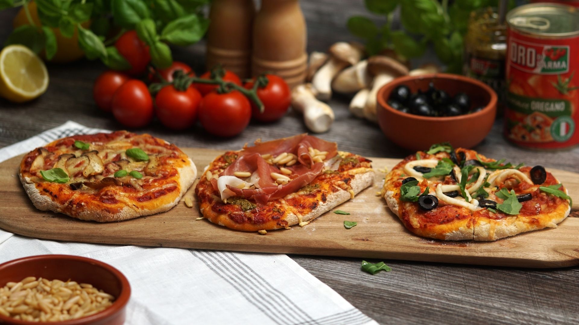 Drei Mini-Pizzen mit verschiedenem Belag auf einem langen Holzbrett angerichtet