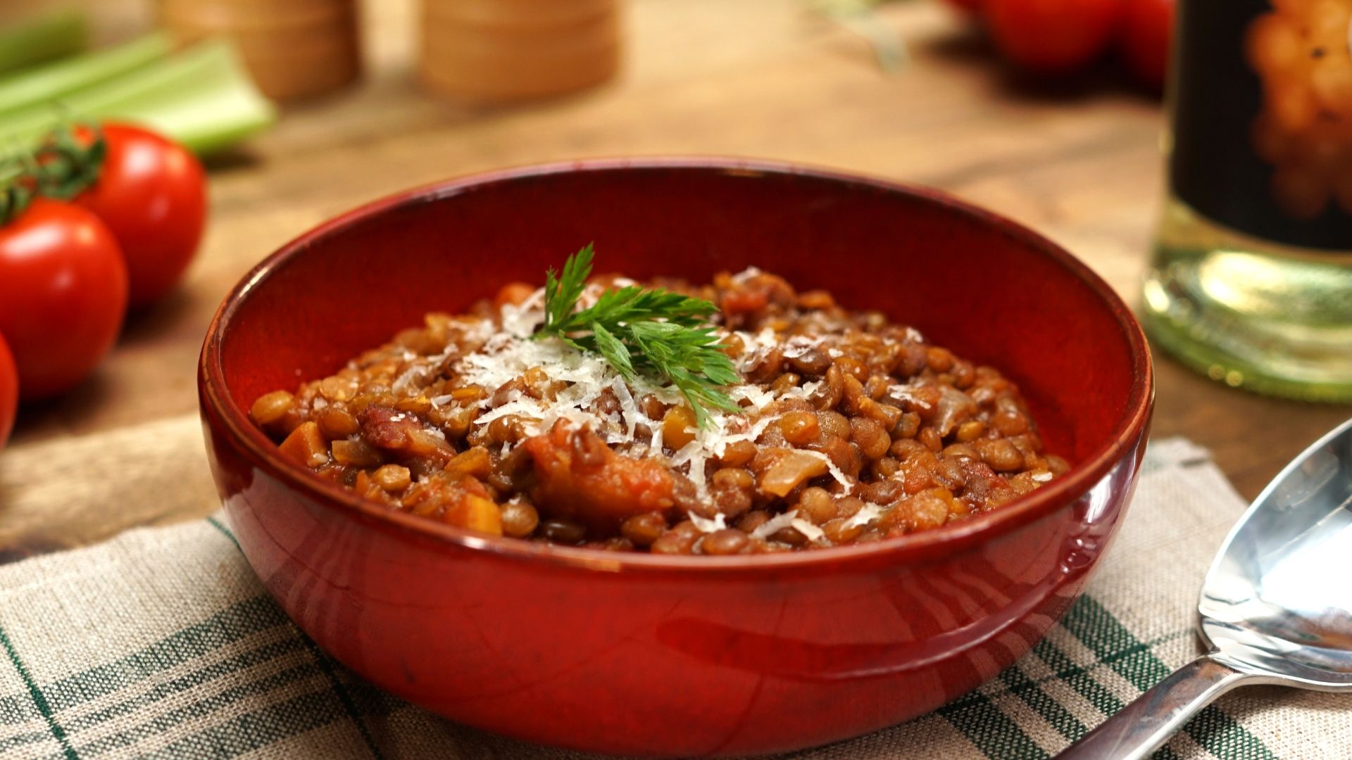 In einer Suppenschüssel ist ein italienischer Linseneintopf. Im Hintergrund liegen Tomaten, ein Salz- und Pfefferstreuer und eine Flasche Essig.