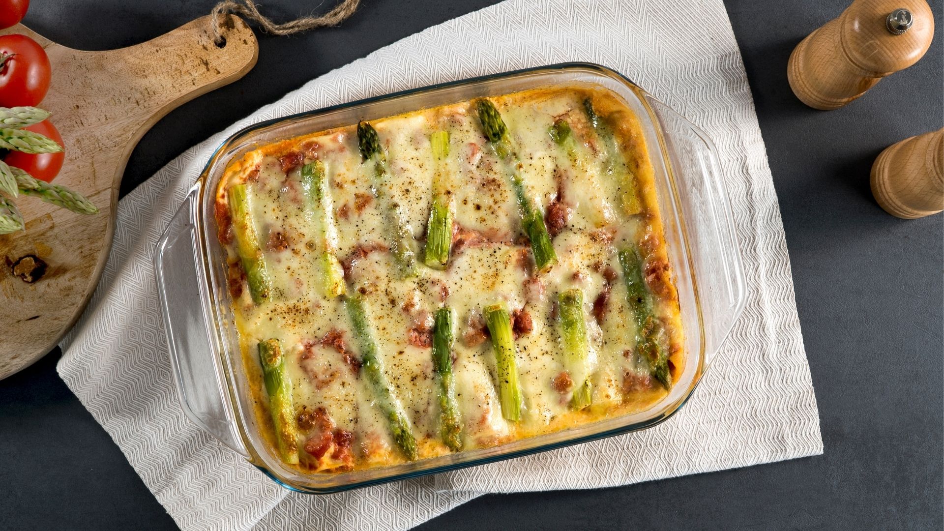 Lasagne mit grünem Spargel in einer durchsichtigen Auflaufform auf einem weißen Geschirrtuch. 